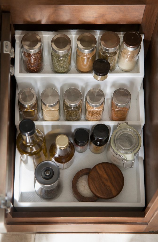 Three-tier shelf organizer holding spice jars in a cabinet.